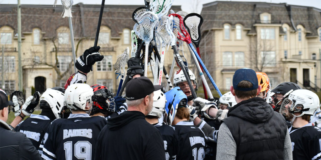Varisty Boys Lacrosse Team in a hudle holding up crosses in celebration