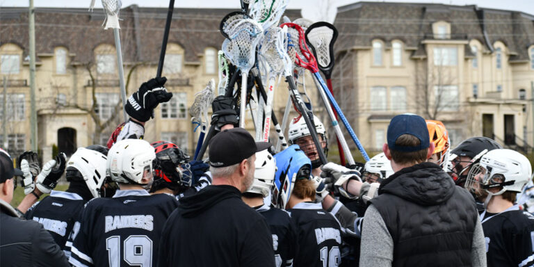 Varisty Boys Lacrosse Team in a hudle holding up crosses in celebration